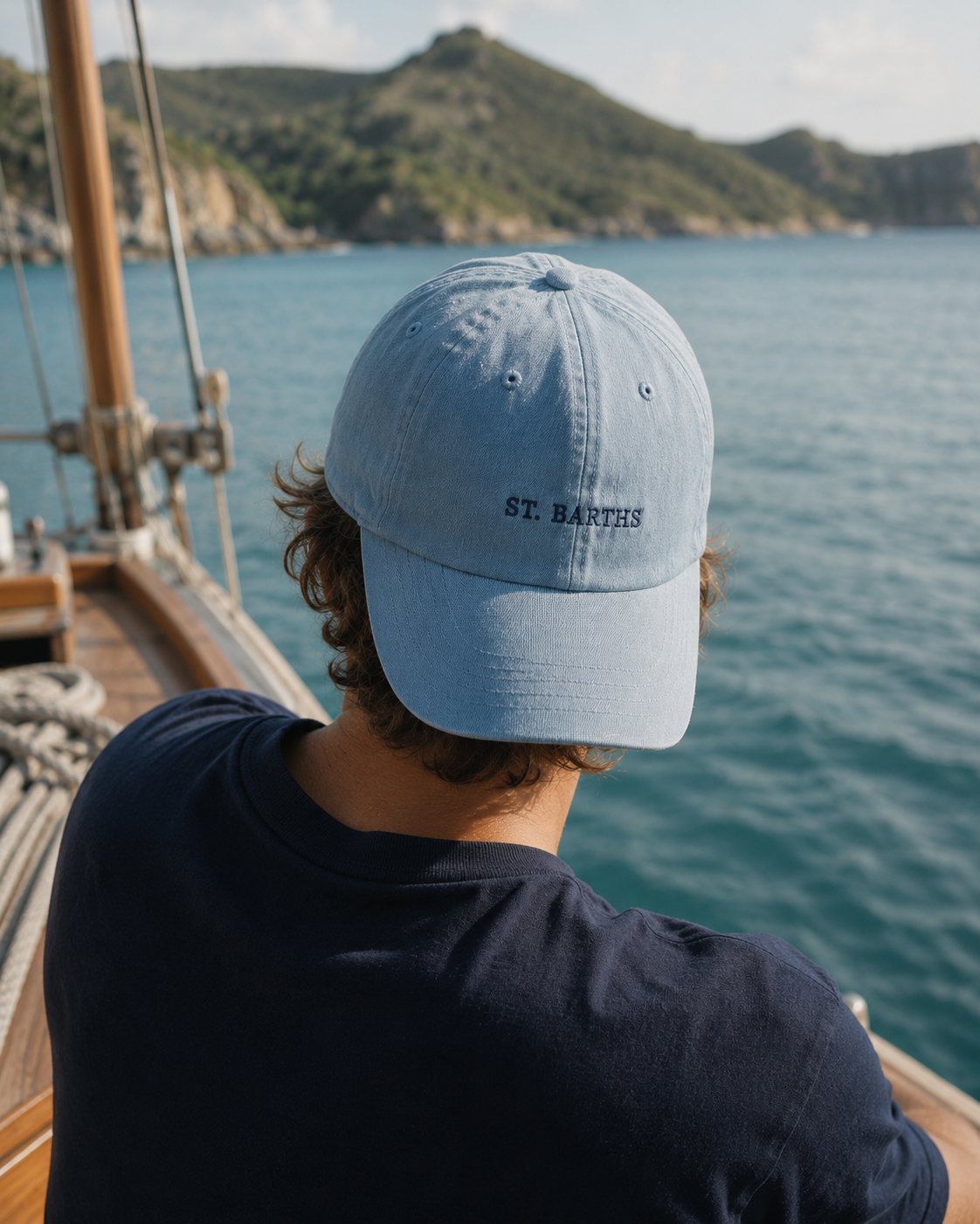 A man in a sky-blue Saline cap looking out from the bow of a sloop in Grand Cul de Sac